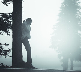 Depressive Frau am Baum lehnend im Nebel
