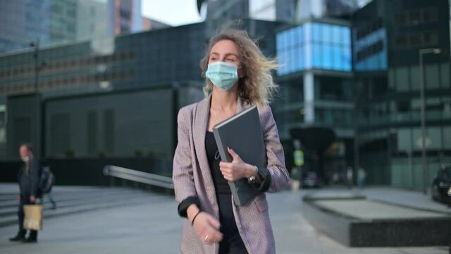 A young business woman walks through the city wearing a medical mask and holding a folder of documents. The need to wear a mask due to an illness or epidemic. Suspicious woman is afraid of getting inf