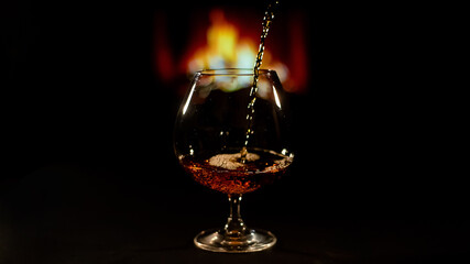 Fototapeta na wymiar Pour brandy into a glass against the background of the fireplace