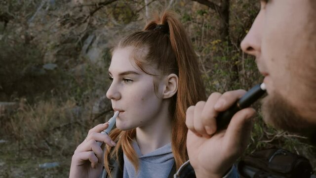 young couple smokes electronic cigarettes, vaping. inhale and blow smoke from mouth.E-cigs,iqos cigarette