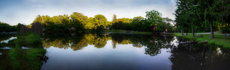A panoramic view of a pond reflecting the trees and blue sky near the small Ontario town of Port Rowan on a beautiful summer evening.