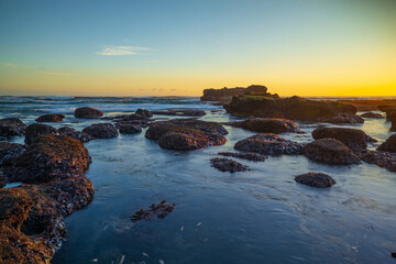 Beach during low tide. Amazing seascape. Stones covered by water. Sunset time. Golden hour. Slow shutter speed. Soft focus. Clear sky. Mengening beach, Bali, Indonesia