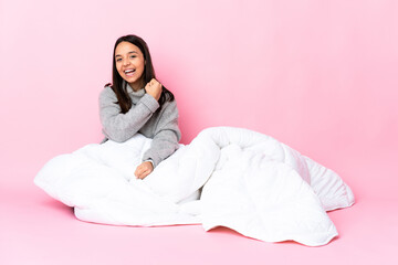 Young mixed race woman wearing pijama sitting on the floor celebrating a victory