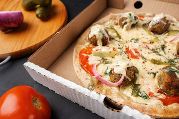 Vegetarian pizza with falafel on whole-wheat flour dough in a cardboard box next to the ingredients, close-up