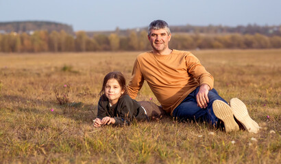 Naklejka na ściany i meble Father and daughter sitting on the grass in a field at sunset.
