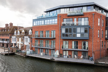 Modern apartment building beside traditional British terraced houses along a river on a cloudy...