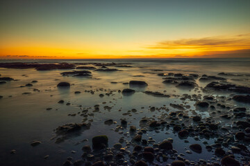Beach during low tide. Amazing seascape. Stones covered by water. Sunset time. Golden hour. Slow shutter speed. Soft focus. Mengening beach, Bali, Indonesia