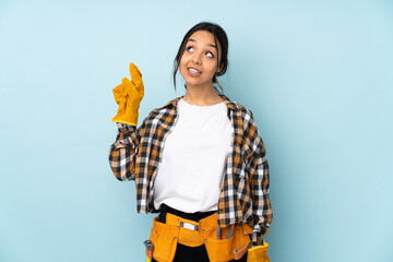 Young electrician woman isolated on blue background with fingers crossing and wishing the best