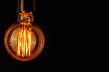 Vintage light bulb on black background, copy space. Glowing edison bulb