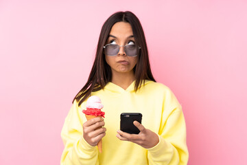 Young brunette girl holding a cornet ice cream over isolated pink background thinking and sending a...