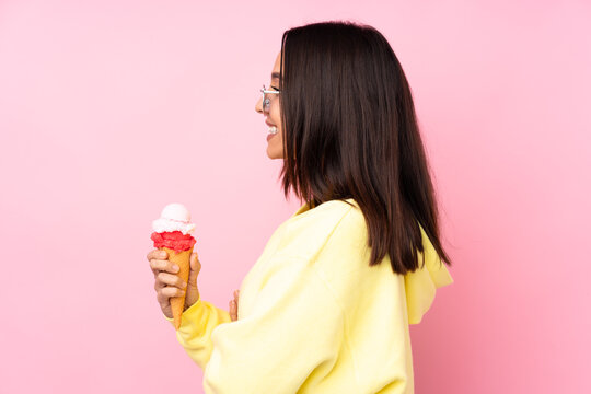 Young brunette girl holding a cornet ice cream over isolated pink background in lateral position