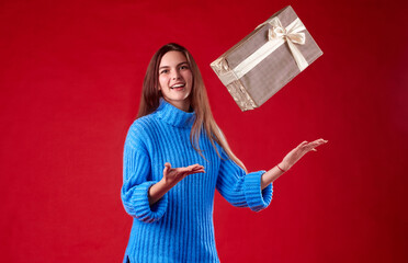  girl in a blue sweater catches gifts in the air on a red background.