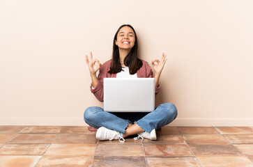 Young mixed race woman with a laptop sitting on the floor in zen pose