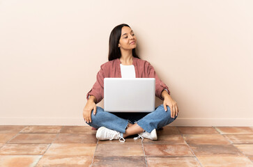 Young mixed race woman with a laptop sitting on the floor . Portrait