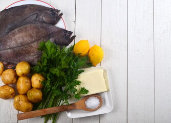 Two whole fresh flounder, potatoes, butter, parsley, lemon, salt on white plate on white wooden background. Copy space. Ingredients for Sole Meunière recipe