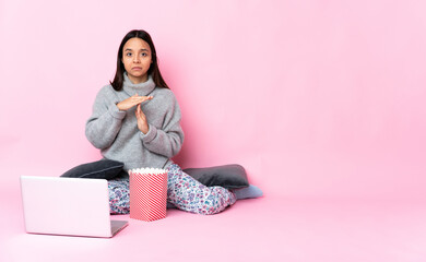 Young mixed race woman eating popcorn while watching a movie on the laptop making time out gesture