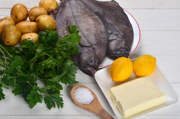 Two whole fresh flounder, potatoes, butter, parsley, lemon, salt on white plate on white wooden background. Copy space. Ingredients for Sole Meunière recipe