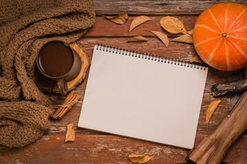 blank paper notebook for text on autumn wooden background, mug of hot drink, coffee, dry yellow leaves, pine cone, pumpkin, copy space for text, top view
