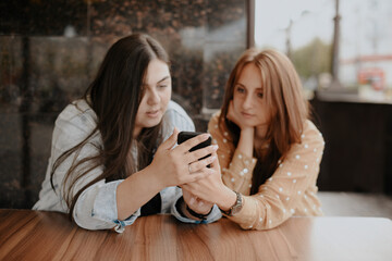 Two young women sit in an open cafe in the city with a phone