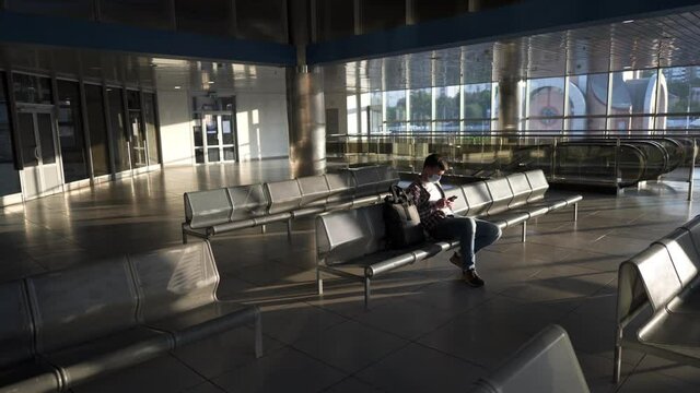 Waiting for flight at an empty airport. Man sitting on chair in empty airport lounge. Flights canceled. Problems with flights during quarantine. The collapse of airlines. Covid 19, coronaviruse
