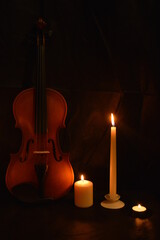 Group of burning candles and violin on black background.