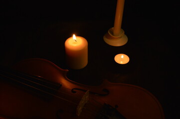 Group of burning candles and violin on black background.