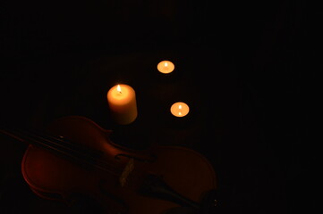 Group of burning candles and violin on black background.