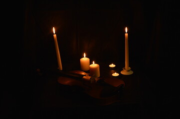 Group of burning candles and violin on black background.