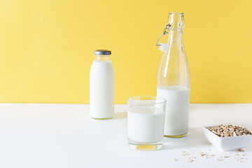 Vegan oat milk on white table over yellow wall.