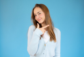 Pretty girl smiling pointing finger right on blue background.