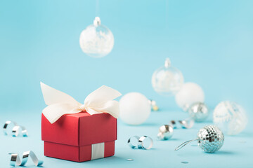 Obraz na płótnie Canvas Christmas card with red Xmas gift box, silver decorations, mirror disco balls on light blue background.
