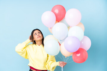 Fototapeta na wymiar Woman holding balloons in a party over isolated blue background having doubts and with confuse face expression