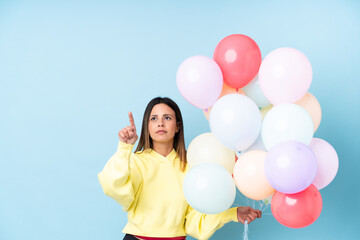 Woman holding balloons in a party over isolated blue background touching on transparent screen