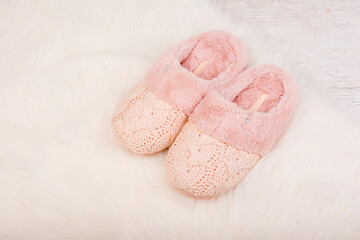 Pair of warm female slippers on white furry carpet
