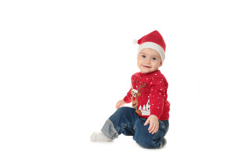 Adorable child is sitting on floor, wearing red Christmas hat, isolated over white