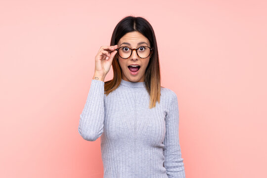 Woman over isolated pink background with glasses and surprised