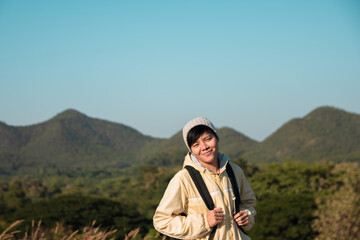 Smiling Asian young man in Long-sleeved shirt and grey hat hiking standing at mountain peak above clouds  Hiker outdoor. Maetip Reservoir Lamphun Province, Northern Thailand Province in the morning.