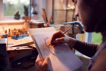 Close Up Of Male Jeweller Sketching Out Design For Ring In Studio