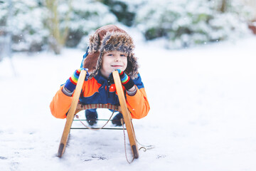 Little kid boy having fung with sleigh ride in winter