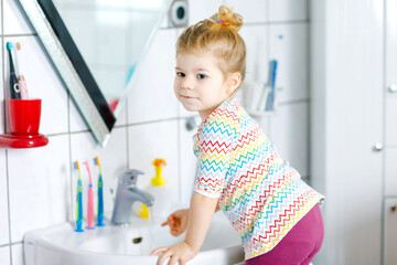 Cute little toddler girl washing hands with soap and water in bathroom. Adorable child learning cleaning body parts. Hygiene routine action during viral desease. kid at home or nursery.