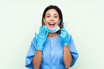 Woman dentist holding tools over isolated green background with surprise facial expression