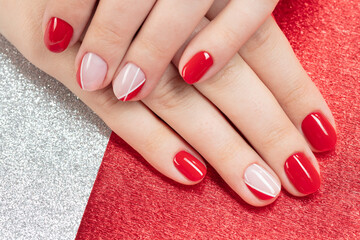Perfect artificial fingernails of young woman. Women's hands with pink, red, white nail Polish applied on a red background. Selective focus
