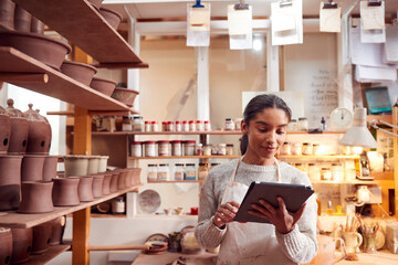 Female Potter In Ceramics Studio Checking Orders Using Digital Tablet