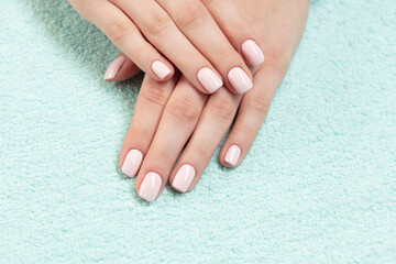 Naklejka premium Female hands with new manicure. Hands with pink nail polish on a colored towel. Care for woman hands. Woman in salon receiving manicure by nail beautician. 