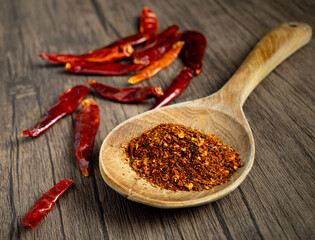 Chili cayenne or crushed dried chili peppers heap in a wooden spoon on a traditional kitchen floor table background with a blur dried chili background.
