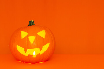 Glowing Halloween pumpkin head jack lantern on trendy orange table background copy space