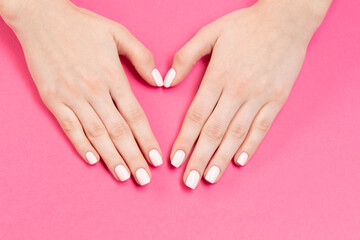 Obraz na płótnie Canvas Hands with pink nail polish on a pink background. Female hands with new manicure. Care for woman hands. Woman in salon receiving manicure by nail beautician.