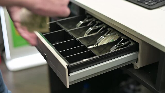 The seller collects cash in the opened cash register of the store, close-up
