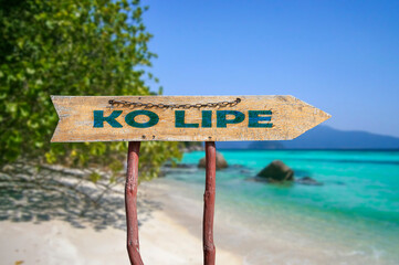 Ko Lipe wooden arrow road sign against tropical beach with white sand and turquoise water background. Travel and relaxation concept.