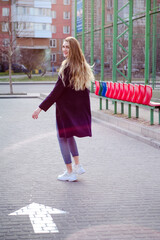 Beautiful young blonde girl in white sneakers and blue coat, having fun, laughing in empty parking lot, near white arrow